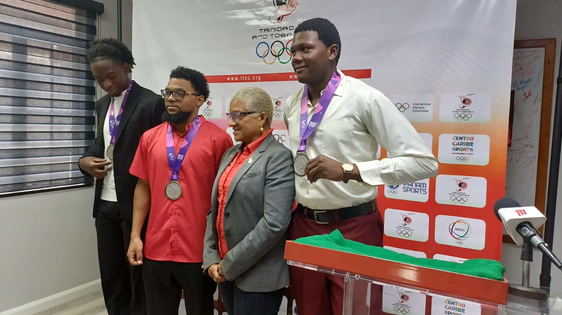 President of the T&T Olympic Committee Diane Henderson, second from right, is flanked by the members of the men’s cycling team which placed third at the Junior Pan Am Games in Asuncion, Paraguay, in 2025, but their medals were upgraded to silver after the winning team was disqualified for doping. The members are Jelani Nedd, left, Ryan D’ Abreau, second from left, and Darnell James, right, as they posed for a photo after receiving their medals yesterday at a ceremony at the Olympic House on Woodford Street, Port-of-Spain.  (Image obtained at guardian.co.tt)
